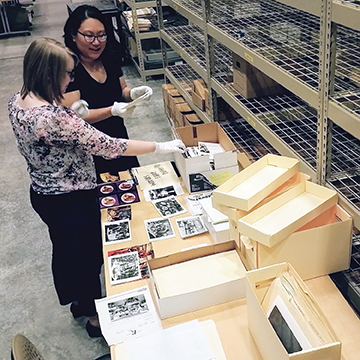 Tammi Kim and student assistant Maggie Bukowski looking at photographs with empty boxes nearby
