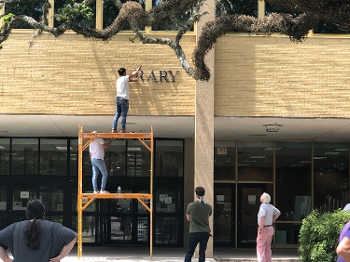 person on ladder removing metal letters from library facade as other people watch