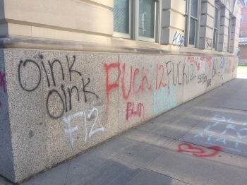 exterior building wall and sidewalk with spray painted messages that read 