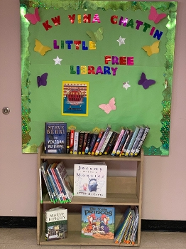 small bookshelf with children's books under green bulletin board wall sign reading