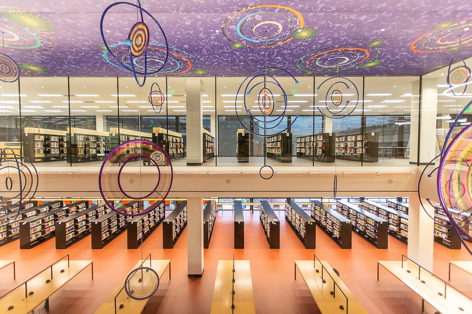 overview of two floors of large interior space with bookshelves and desks, planet-like mobiles hanging from purple ceiling