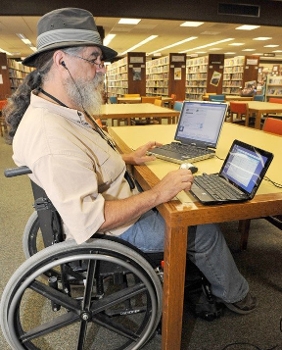 senior man in wheelchair at desk in library with laptop