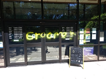 library entrance with GROOMER spray painted across doors in yellow paint, sandwich board to right that reads