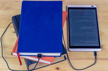e-reader with charging cord plugged into pile of books