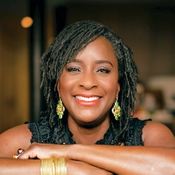 Gena Cox head shot, smiling Black woman with large earrings and locs