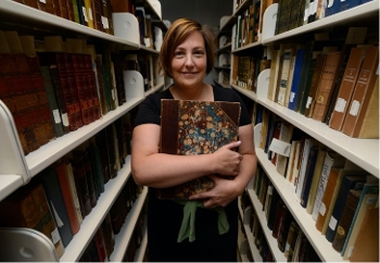 woman standing between stacks shelving holding old book, smiling