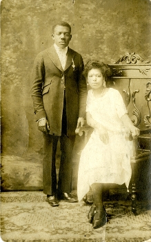 sepia tone postcard showing Black couple, man standing and woman seated