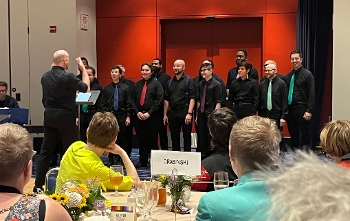 Chicago Gay Men's Choir singing in front of table of people seen from behind