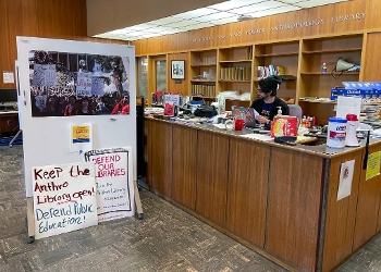 male student at reference desk at anthropology library, protest signs set up on floor