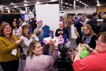 women holding up knitting on a busy show floor