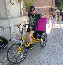 happy woman in sunglasses on yellow book bike with magenta locker on back