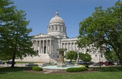 Missouri Capitol building exterior with large trees framing the shot, with a fountain in the foreground