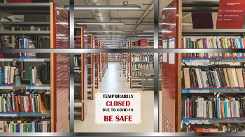 Library shelves holding books with sign across central aisle saying