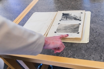 hand pointing at pages in display case showing 2 old looking b&w photos of park views