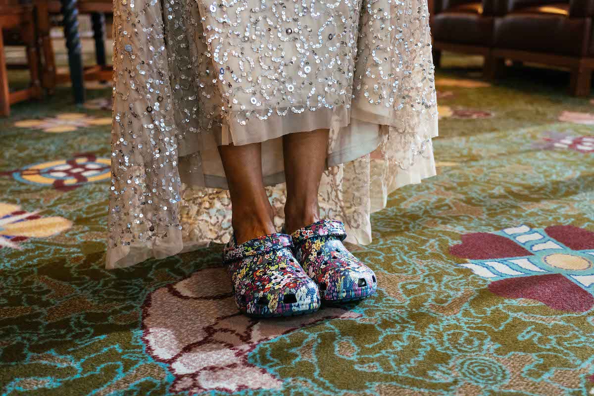 legs emerging from glittery silver long gown, feet in colorful flowered Crocs