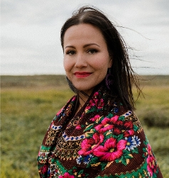 Lindsay Knight head shot, woman with black hair and red lipstick in colorful embroidered shawl, standing against horizon