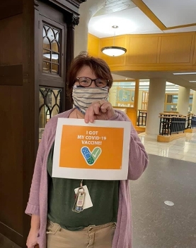 woman in glasses and mask holding sign reading