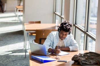 student studying at library desk with windows behind him
