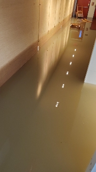 hallway flooded with brown water, chairs overturned at end